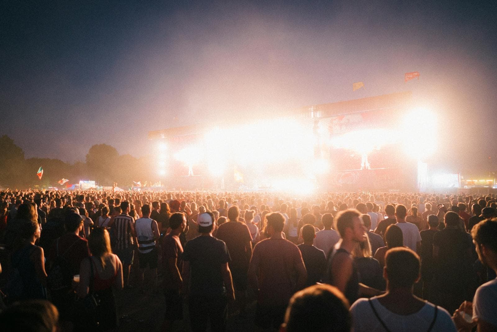Foule devant une grande scène de festival éclairée de nuit, matériel événementiel installé en plein air